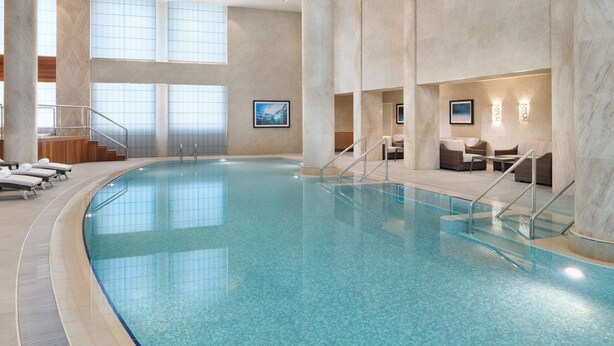 Una gran piscina interior amb aigua transparent de color blau, envoltada de parets i columnes de marbre. Hi ha gandules i una escala que condueix a un nivell superior.