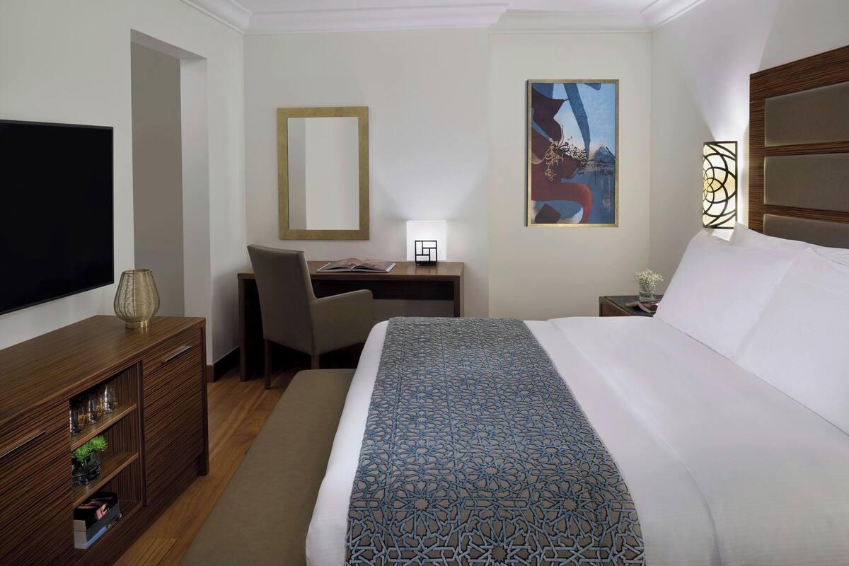 A hotel room with a large bed, a desk, a chair, a TV, and a mirror.