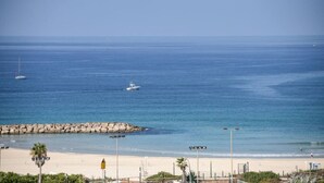 Een strand met een rotsachtige zeedijk, een zandstrand en enkele boten in het water.