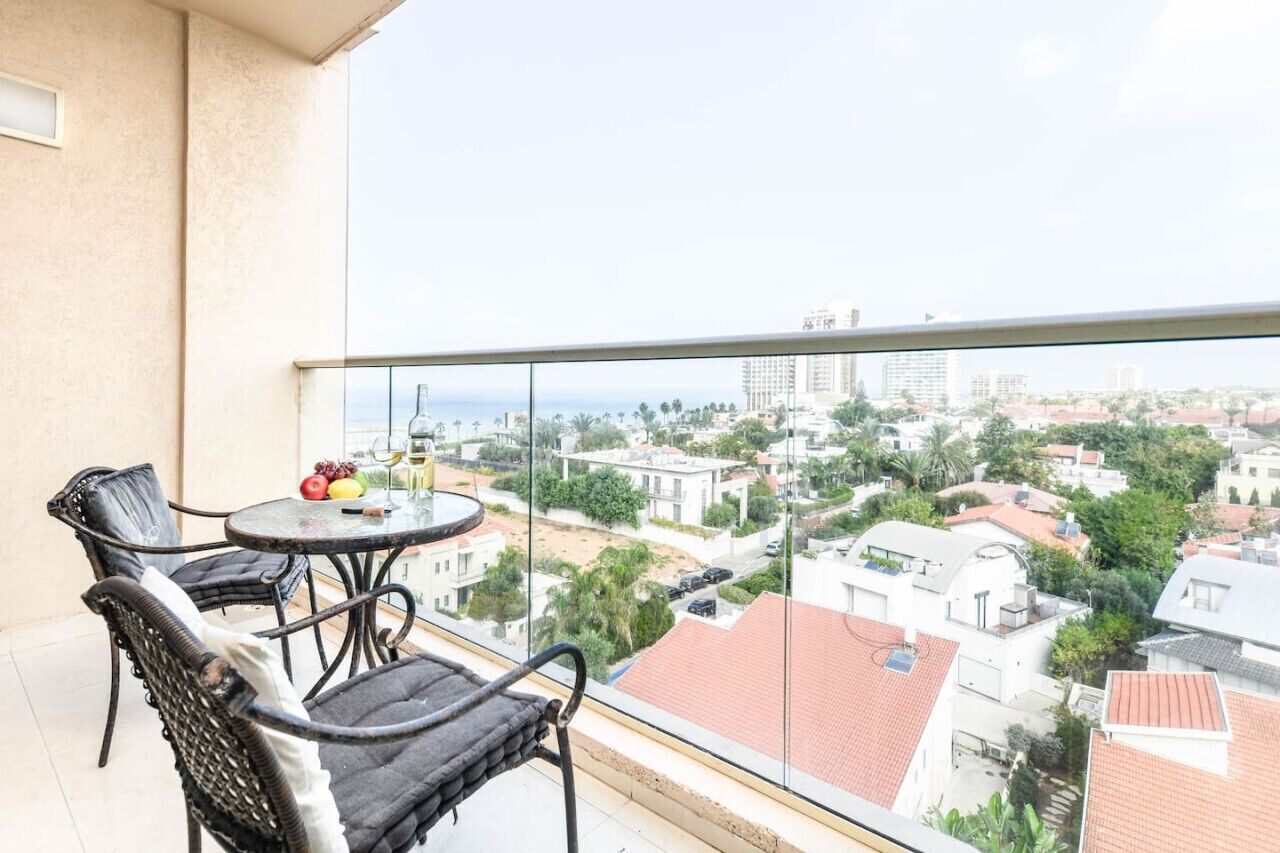 Un balcon avec des fauteuils en osier, une table ronde avec des fruits et un verre, et une vue sur la ville.
