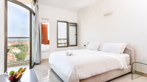 Een hotelkamer met een bed, een raam met gordijnen, uitzicht op gebouwen en een tafel met fruit.
