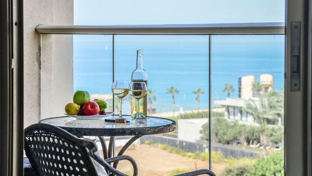 Een balkon met een tafel gedekt voor twee personen, inclusief een fles en glazen, en een selectie fruit.