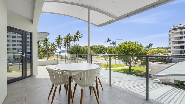A balcony with a white table and chairs, overlooking a street with palm trees and buildings. - Healthy Living Centre (Cairns North)