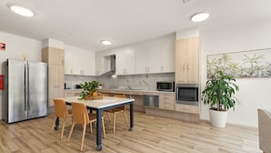 A modern kitchen with a dining area, featuring a stainless steel refrigerator, wooden cabinets, and a potted plant. - Healthy Living Centre (Cairns North)