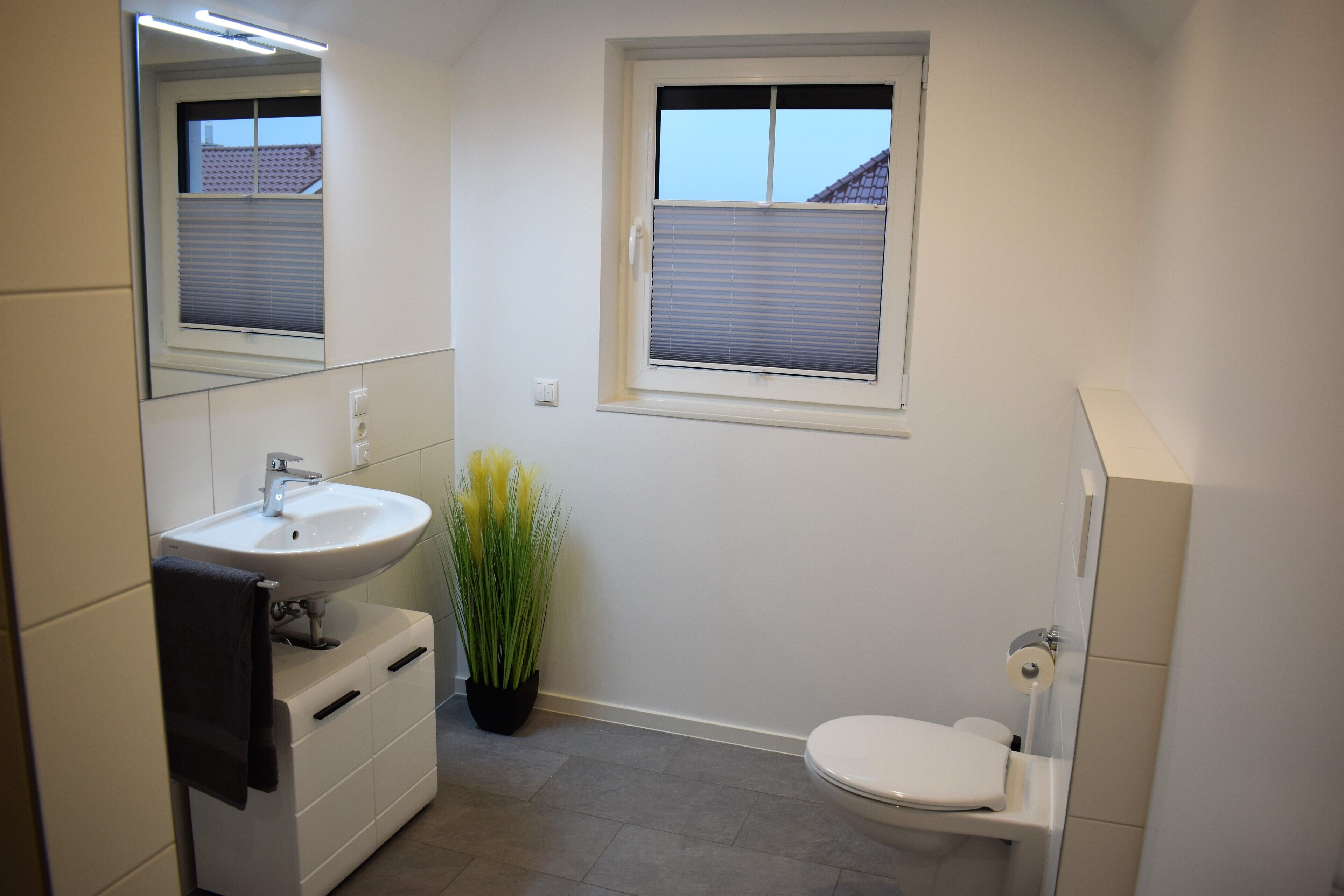 A bathroom with a white sink, mirror, toilet, and a window with blinds.