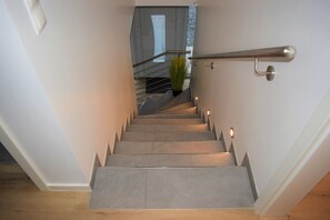 Un escalier moderne avec une rampe, des marches recouvertes de moquette et un pot de fleurs placé en haut.