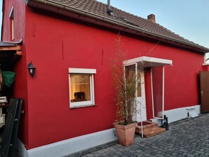 Un bâtiment rouge avec une petite fenêtre, une porte et un pot de fleurs.