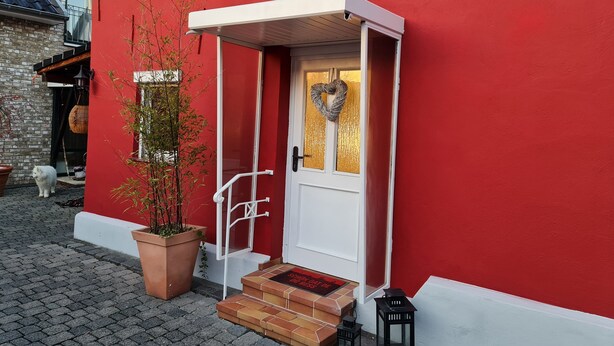 Un edificio rojo con una puerta blanca, una decoración con forma de corazón y una planta en maceta.