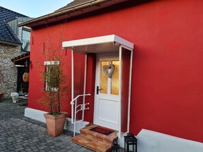 A red building with a white door, a heart-shaped decoration, and a potted plant.