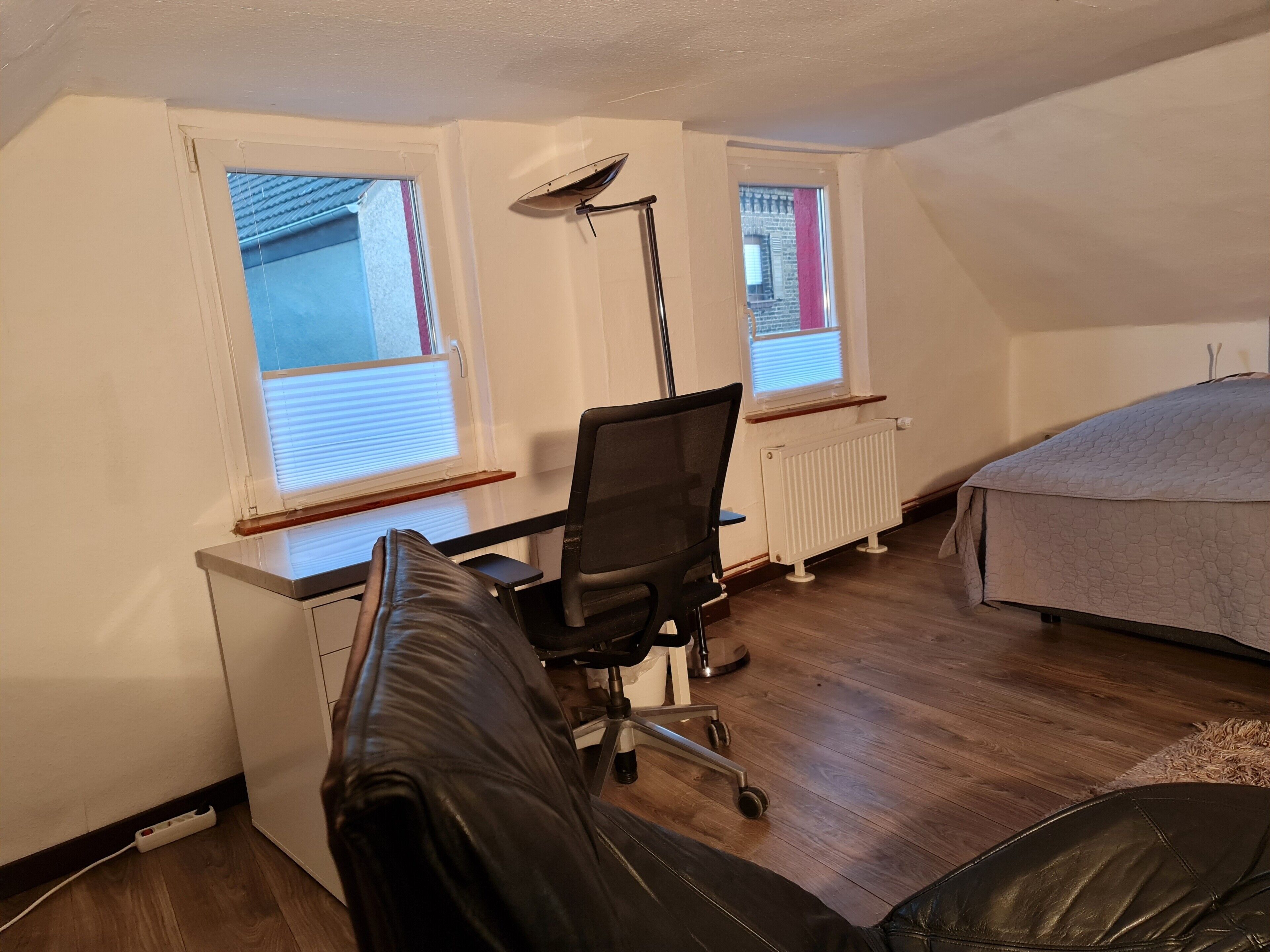 Ein Zimmer mit Schreibtisch, Stuhl, Heizkörper und einem Bett.