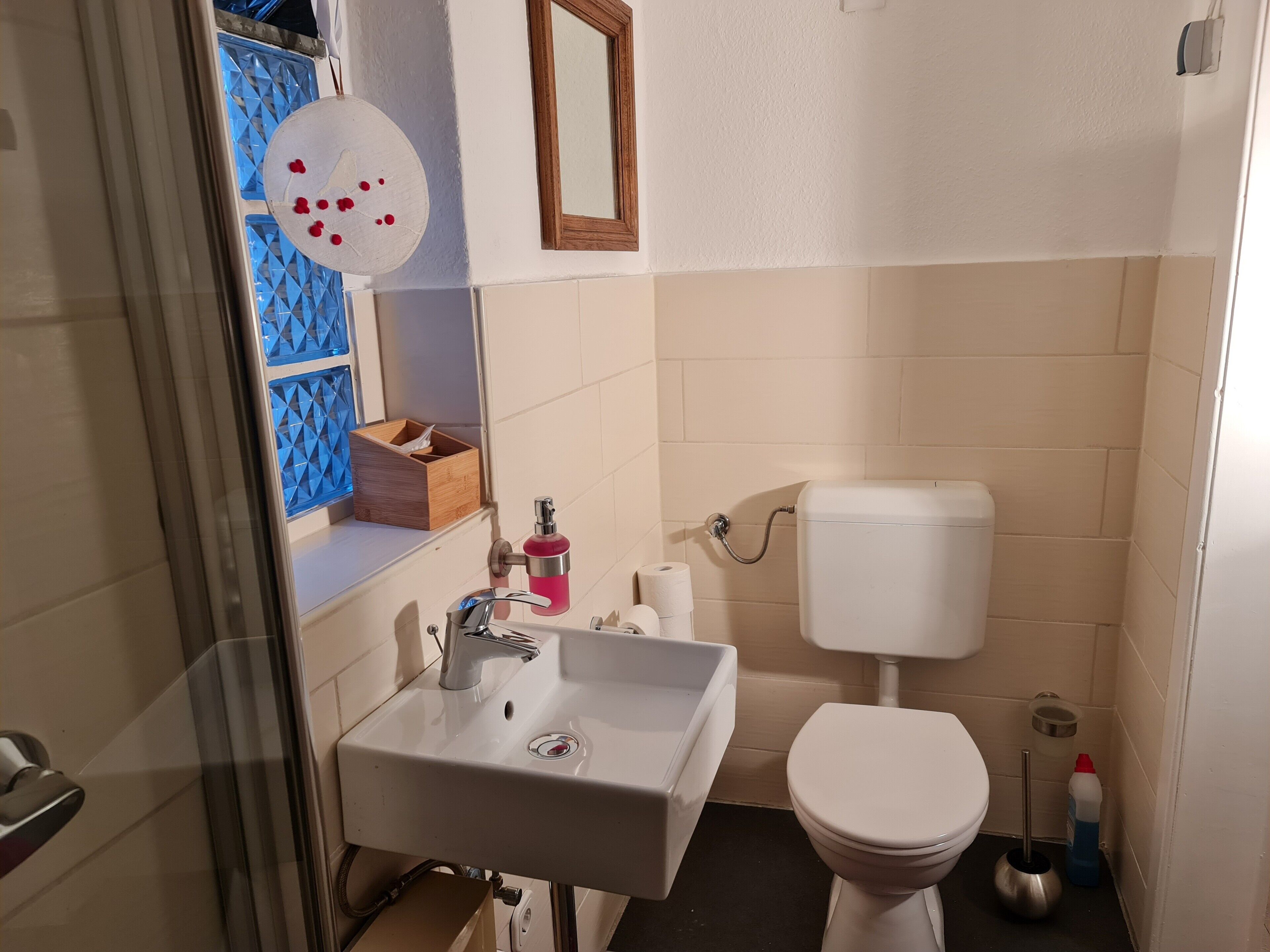 Un baño con lavamanos blanco, inodoro, espejo y un adorno azul en la pared.