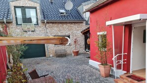 Un patio con un edificio rojo, una mesa de madera, plantas en macetas y una antena parabólica.