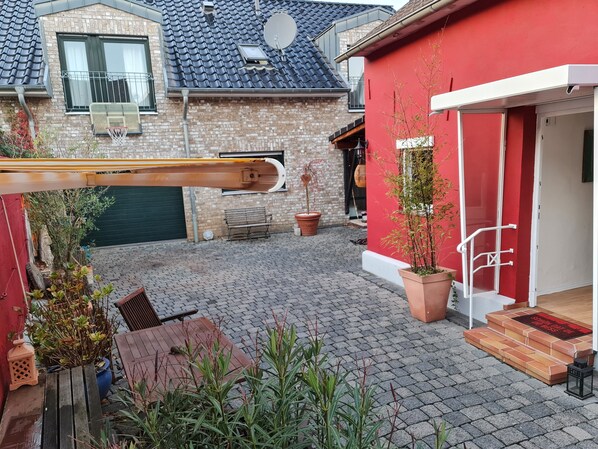 Une cour avec un bâtiment rouge, une table en bois, des plantes en pot et une antenne parabolique.