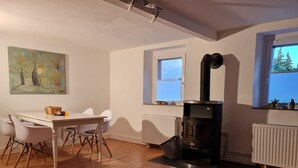 Una sala de estar moderna con comedor, una estufa de leña negra, paredes blancas y un cuadro.