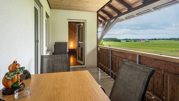 Eine Holzterrasse mit Blick auf ein grünes Feld, ein Esstisch mit Stühlen und eine kleine Kürbisdekoration.