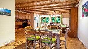 Ein Essbereich mit Holzbänken und einem Glastisch, Holzbalken an der Decke und Blick auf Grünflächen.