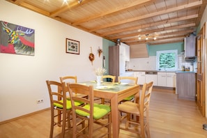 Un coin repas avec une table et des chaises en bois, une cuisine en arrière-plan et un tableau accroché au mur.