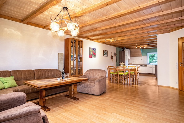 Un vaste espace de vie doté d’un plafond en bois, d’une table à manger avec des chaises, d’un canapé et d’un meuble.