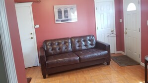 A room with a brown leather sofa, a white door, a white door with a window, and a wall-mounted picture.