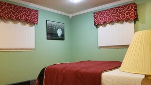 A room with two windows, each with a red and white valance, a bed with a red bedspread, a lamp, and a framed picture on the wall.