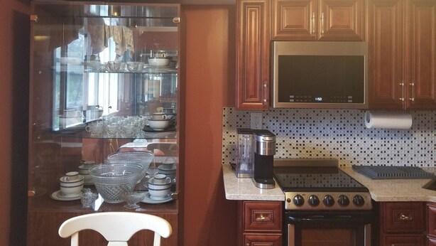 A kitchen with wooden cabinets, a stainless steel stove, a microwave, and a glass display cabinet with dishes.