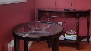 A room with a TV mounted on the wall, a glass table, and a wooden table with books.