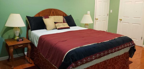 A bedroom with a bed, two bedside lamps, a bedside table with a clock, and a door. - Relax and rejuvenate in this Hideaway Apartment close to public transportation . (North Baldwin)