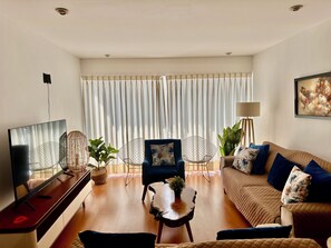 Una sala de estar con un sofá, un televisor, una mesa de centro y una silla.