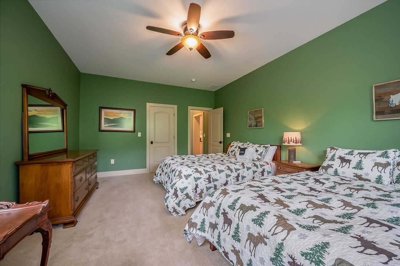 A bedroom with two beds, a ceiling fan, a dresser, and a nightstand with a lamp.