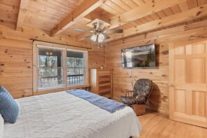 Relax in this serene bedroom with a large bed, ceiling fan, and TV, offering a peaceful view of the outdoors.