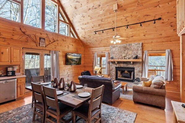 A cozy cabin interior with a dining area, a fireplace, and a stone wall.