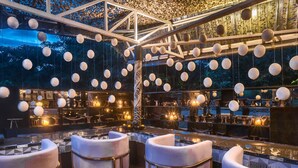 Zona de bar con asientos acolchados blancos y luces esféricas colgantes.