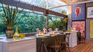 Un espacio exterior con mesas y sillas de madera, y plantas en macetas.