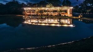 Un espacio exterior bien iluminado con piscina, mobiliario y una estructura con luces reflejándose en el agua.