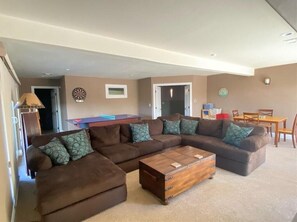 A living room with a sectional sofa, a wooden coffee table, and a dartboard on the wall.