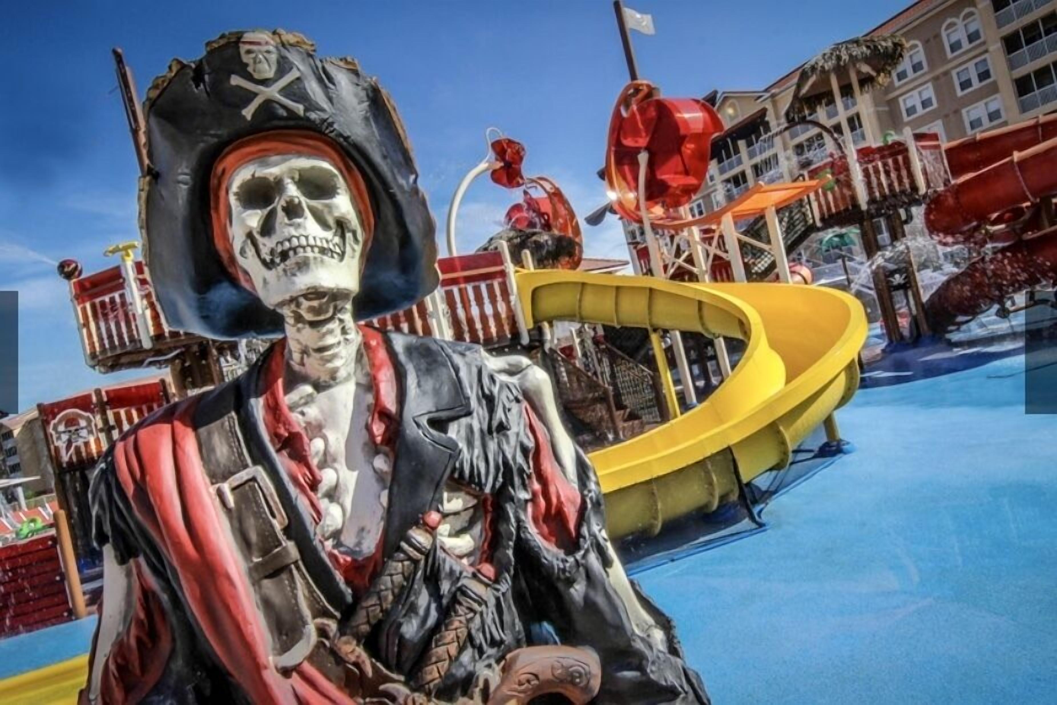 Eine Skelettrpiratenfigur in einem Spielplatzbereich mit Rutschen und einem Gebäude im Hintergrund.