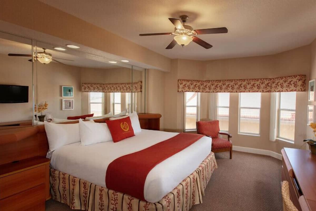 A hotel room with a large bed, a desk, a chair, a television, and a ceiling fan.