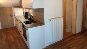 Een kleine keuken met witte kastjes, een inbouwfornuis, een koffiezetapparaat en een radiator.