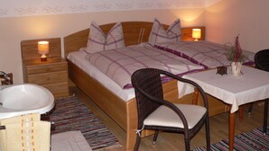 Een slaapkamer met een houten bed, bedlampen, een rieten stoel, een kleine tafel en een badkamer met een wastafel en bad.