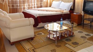 Una habitación de hotel con cama, sofá, mesa de centro de vidrio y televisión.