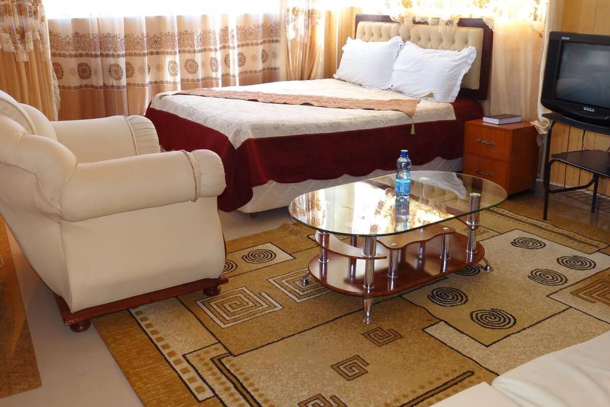 A hotel room with a bed, a sofa, a glass coffee table, and a television.
