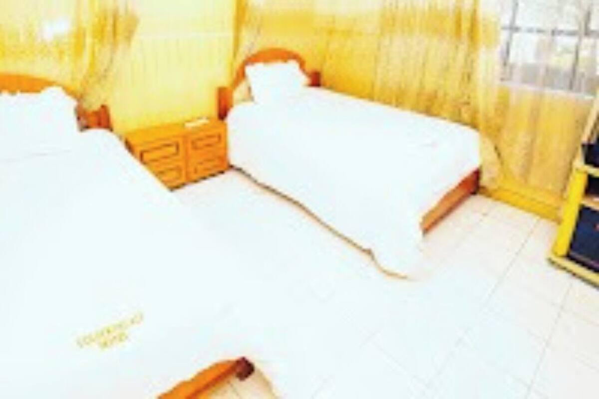 A room with two beds, a wooden headboard, and a window with yellow curtains.