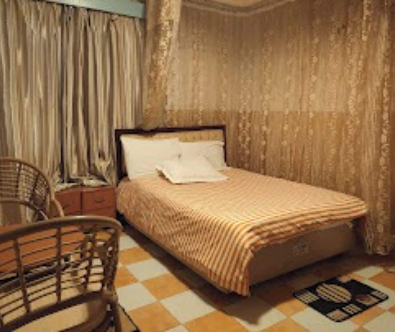 A bedroom with a bed, a nightstand, a chair, and a checkered floor.