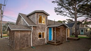 A two-story wooden house with a sloped roof, a blue door, and a small porch. - Exquisitely Maintained Cottage Inside and Out, Open Layout, One Block to Beach,  *Pet Friendly* (Rockaway Beach)