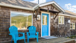 A wooden cabin with a blue door and two blue Adirondack chairs on a wooden deck. - Exquisitely Maintained Cottage Inside and Out, Open Layout, One Block to Beach,  *Pet Friendly* (Rockaway Beach)