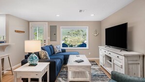 A living room with a sofa, coffee table, TV, and a view of the outdoors. - Exquisitely Maintained Cottage Inside and Out, Open Layout, One Block to Beach,  *Pet Friendly* (Rockaway Beach)
