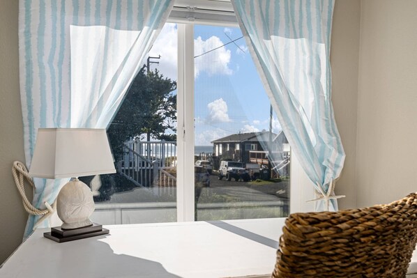 A room with a view of a house and a car through a window with light blue curtains. - Exquisitely Maintained Cottage Inside and Out, Open Layout, One Block to Beach, *Pet Friendly* (Rockaway Beach)