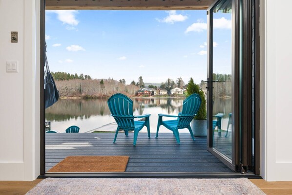 Une terrasse avec deux chaises et une table, donnant sur un lac, avec des maisons en arrière-plan.