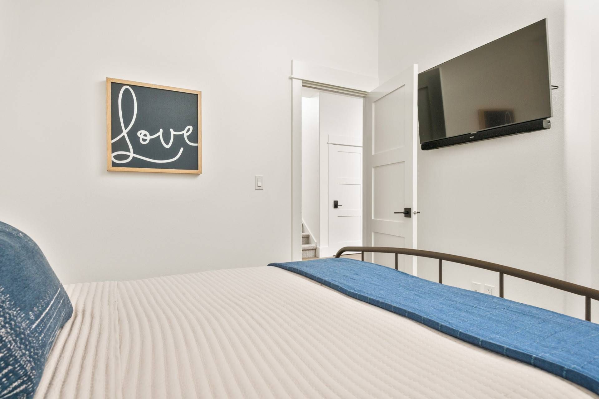 A bedroom with a bed, a TV mounted on the wall, and a door leading to another room.