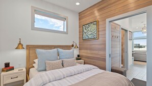 A bedroom with a wooden headboard, a large window, a bedside table with a lamp, and a view of the outside. - Bayfront Tiny Home - Tillamook Bay/Garibaldi (Garibaldi)